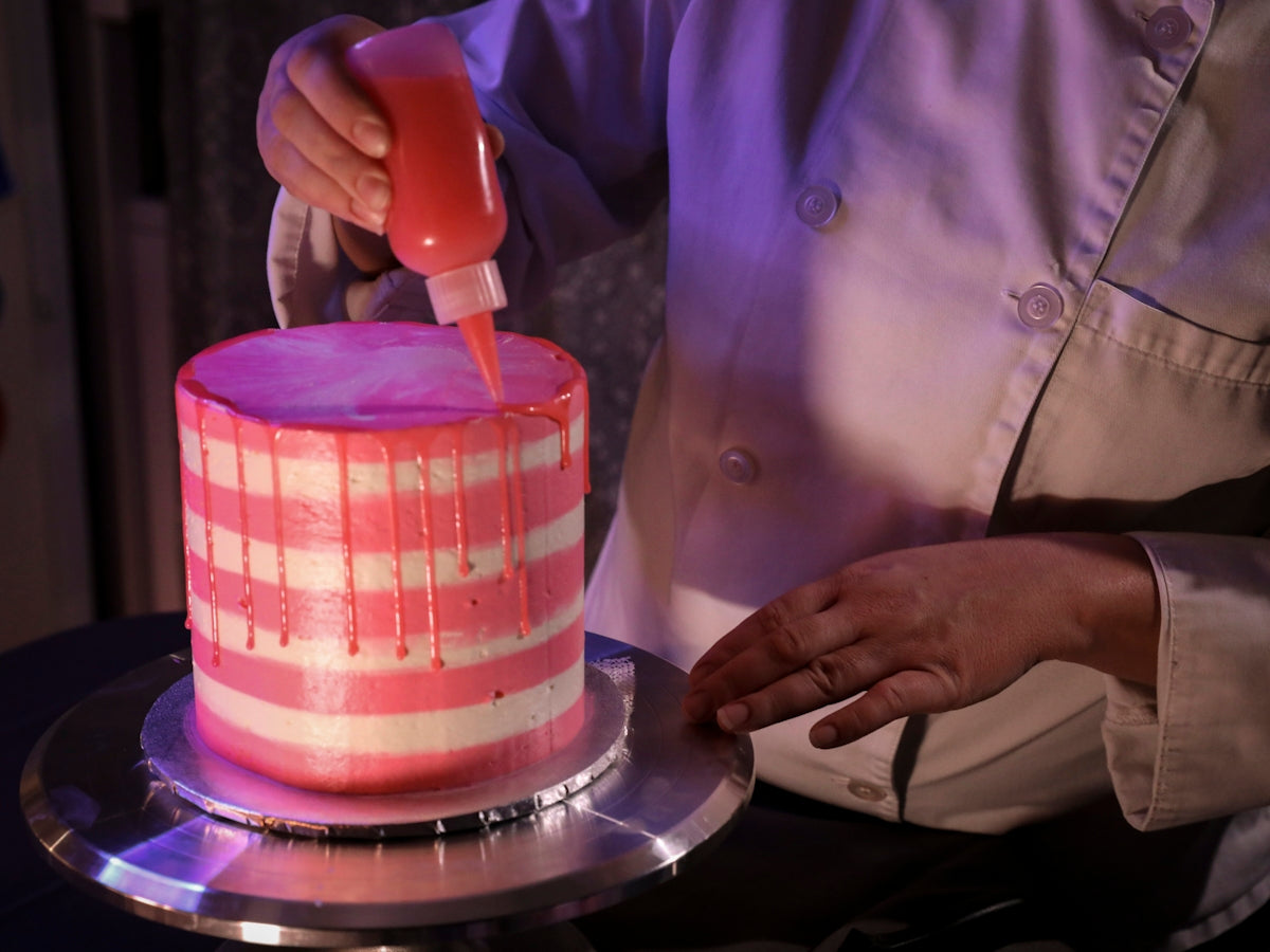 a person is decorating a cake with pink icing