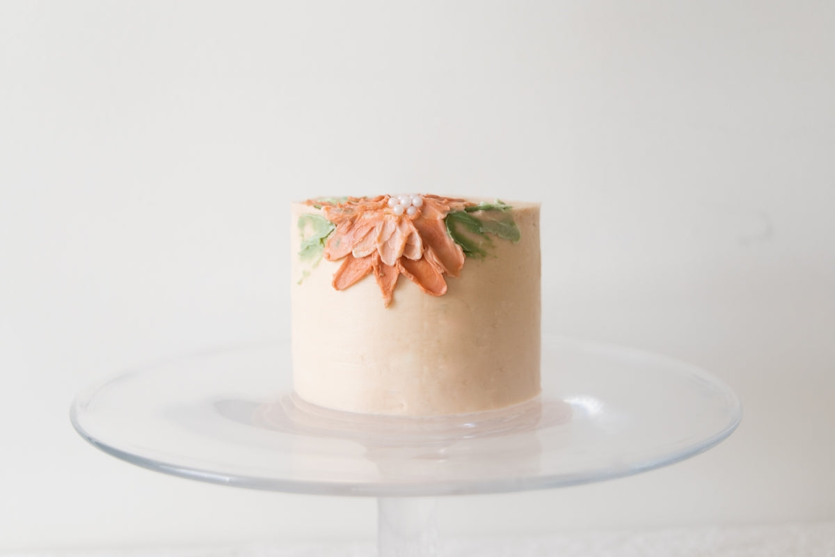 a white cake with orange flowers on a clear cake plate