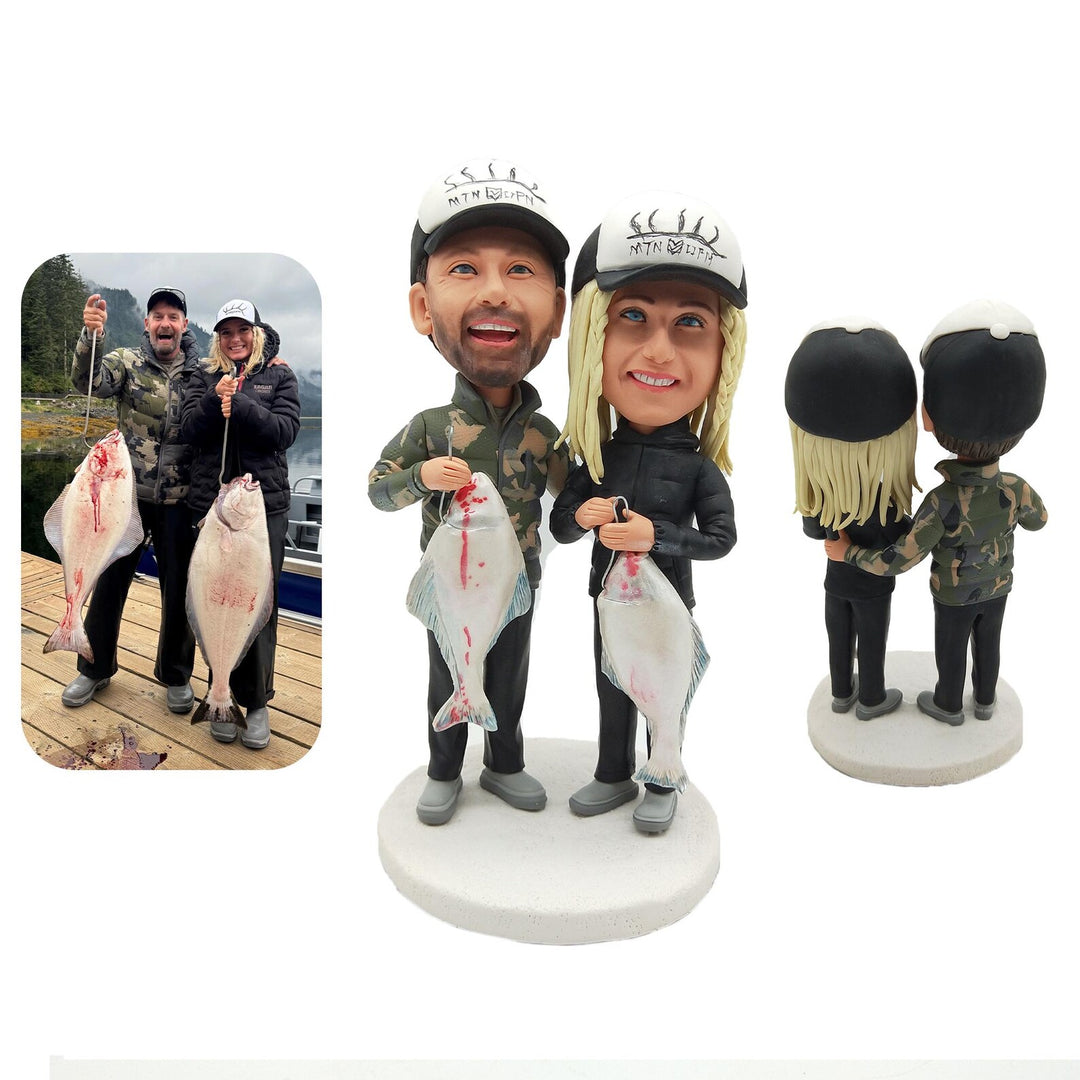 Bobblehead figures of a couple holding fish with a photo of them fishing on a dock.